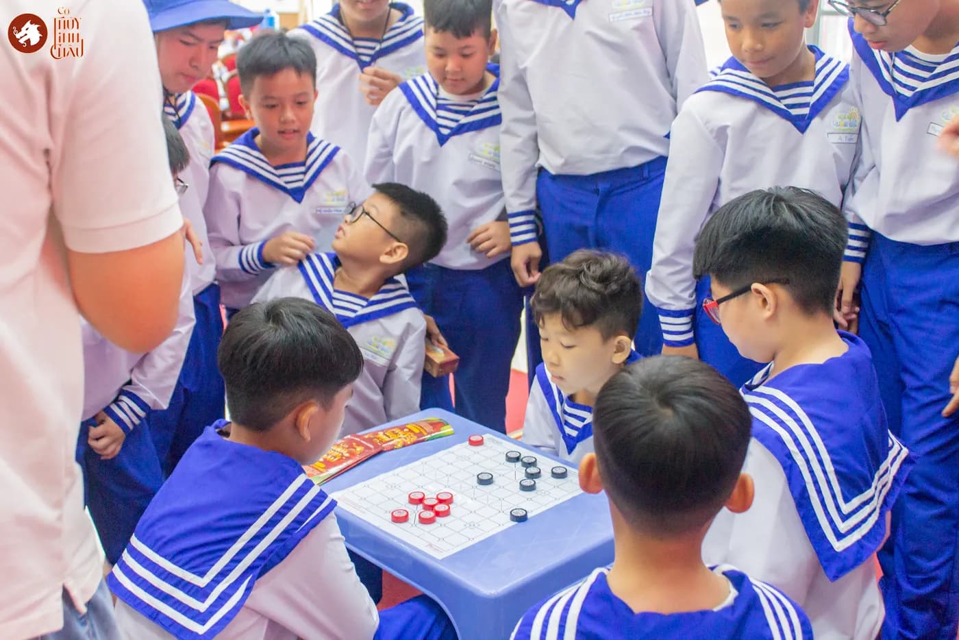 Hình ảnh các em tham gia trận đấu cùng những người bao quanh theo dõi khi chơi cờ Thủy Tinh Châu.