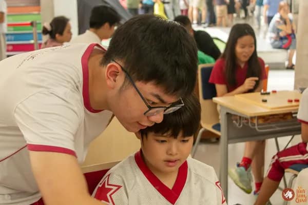 Hình ảnh bạn học sinh Trường Vietnam Australia International School hướng dẫn em nhỏ chơi Cờ Thủy Tinh Châu trong sự kiện VAS OMLYMPIC 2026